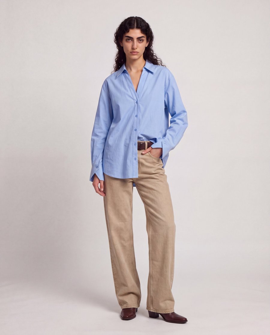 Studio image of a model in the blue shirt and beige wide-leg jeans, one hand in her pocket