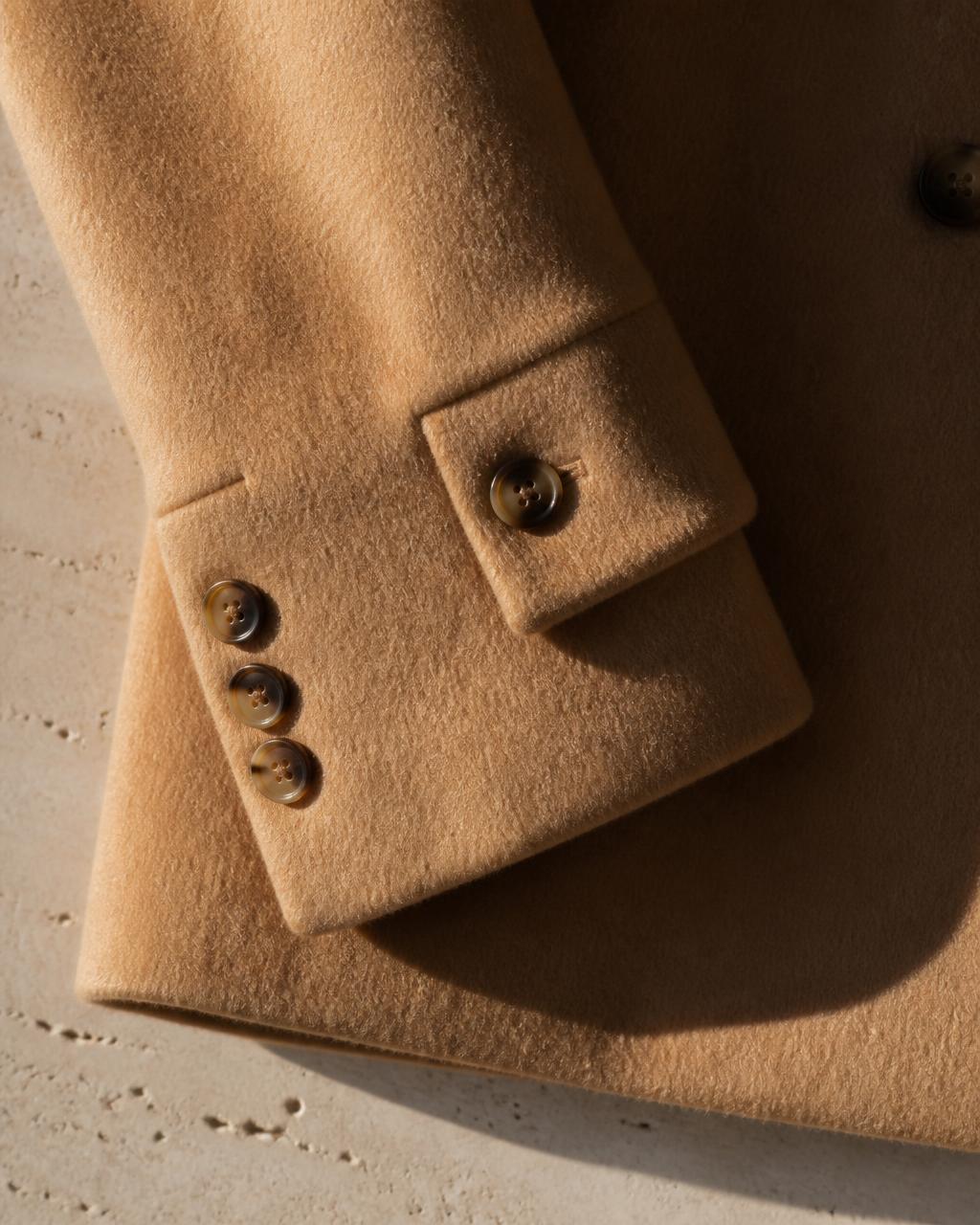 Cuff and horn buttons of a camel wool coat on pale travertine