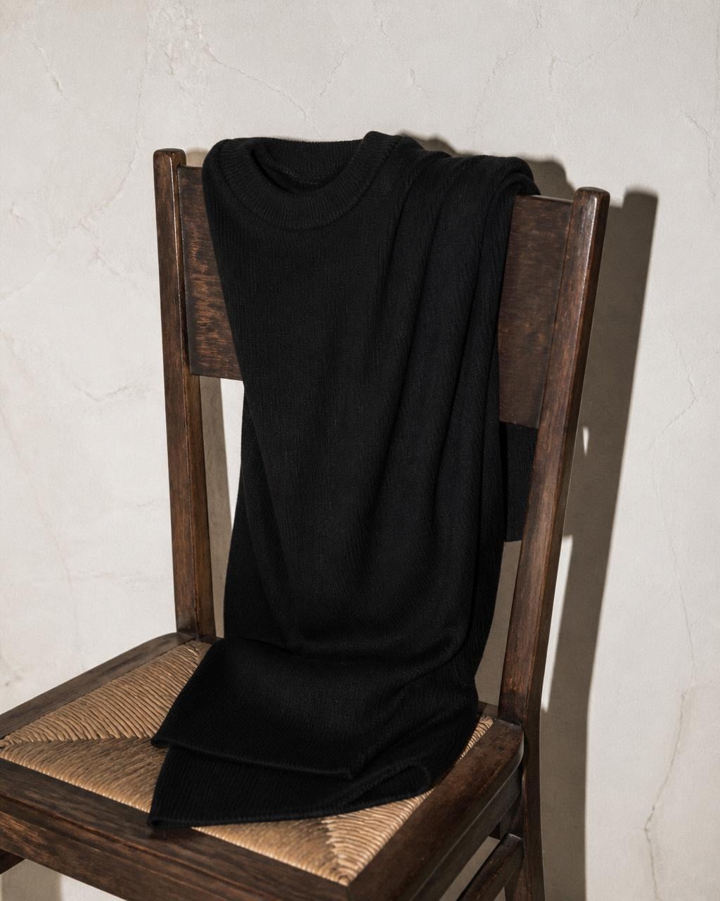 Waist of a black knit dress against pale plaster