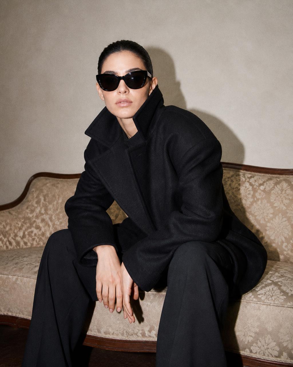 The same model leaning forward on the sofa, collar popped, under direct flash